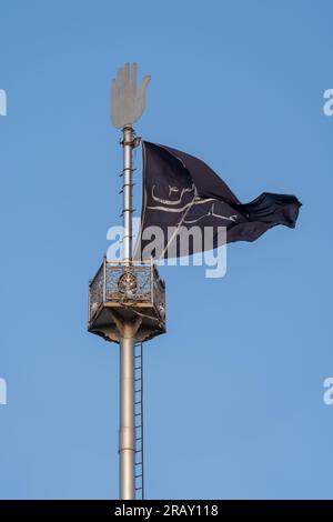 Bhit Shah, Sindh, Pakistan - 11 16 2019 : Schwarze schiitische muslimische Flagge auf einem Mast mit silbernem hamsa auf blauem Himmel Hintergrund, Schah Abdul Latif Bhittai Schrein Stockfoto