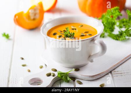 Kürbissuppe mit Kürbiskernen auf weißem Schneidebrett Stockfoto