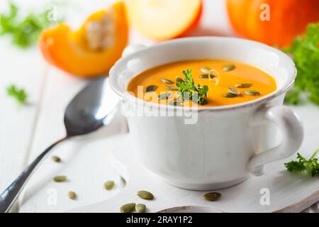Kürbissuppe mit Kürbiskernen auf weißem Schneidebrett Stockfoto