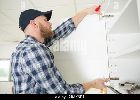 Handwerker, der eine Tür am Schrank repariert Stockfoto