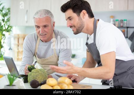 Hipster-Sohn mit seinem Senior-Vater, der in der Küche kocht Stockfoto