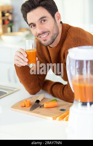 Junger bärtiger Mann trinkt frisch gepressten Karottensaft Stockfoto