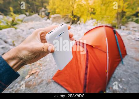 Powerbank zum Aufladen von Smartphones und anderen elektrischen Geräten am Wochenende bei Wanderungen. Orangefarbenes Zelt im Hintergrund Stockfoto