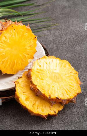 Frisch geschnittene, saftige Ananas auf einem Teller mit dunkelgrauem Tischhintergrund. Stockfoto