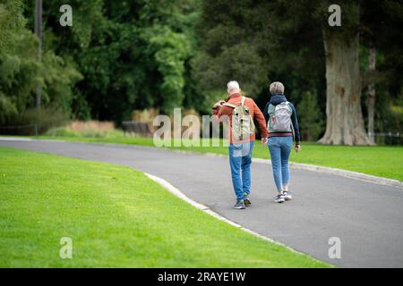 Ein Paar, das in einem Garten spaziert. Mann und Frau gehen in der Natur unter Bäumen, umgeben von Pflanzen. Familie zusammen in einem Park in Stockfoto