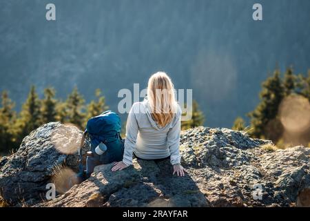 Frau mit Rucksack, die auf einem Felsen ruhte, nachdem sie erfolgreich den Berggipfel erklommen hatte Stockfoto