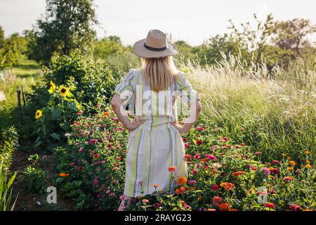 Eine Frau, die im Blumengarten steht. Weibliche Floristin, die sich im Sommer auf der blühenden Blumenfarm entspannen und die Aussicht genießen kann Stockfoto