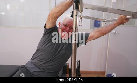 Senior-Mann, der mit Pilates Machine trainiert. Ältere Trainingsprogramm, dehnen Körper und kümmern sich um die Gesundheit der Wirbelsäule Stockfoto