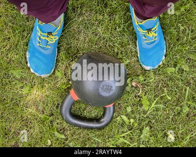 Schwere Eisenhülse und Männerfüße auf dem Rasen, Fitnesskonzept im Garten Stockfoto