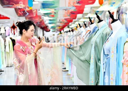 Caoxian, Chinas Provinz Shandong. 6. Juli 2023. Eine Frau wirbt für traditionelle chinesische Hanfu-Kleidung durch Livestreaming auf einem Hanfu-Stützpunkt in Caoxian County, Ostchina-Provinz Shandong, am 6. Juli 2023. Caoxian County hat in den letzten Jahren eine komplette Hanfu-Industriekette aufgebaut. Derzeit gibt es mehr als 2.100 mit Hanfu verbundene Unternehmen im Bezirk. Der Umsatz von Hanfu in Caoxian erreichte in der ersten Jahreshälfte fast 4 Milliarden Yuan (etwa 552 Millionen US-Dollar). Kredit: Guo Xulei/Xinhua/Alamy Live News Stockfoto