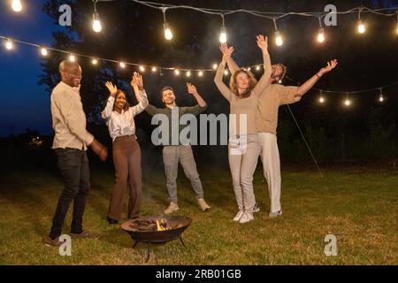 Mehrere ethnische Gruppen von Freunden, die im Garten grillen, lachen und tanzen und einer Gruppe von Freunden zeigen, wie sie sich mit den Sparklern am Abend amüsieren. Hochwertiges Foto Stockfoto