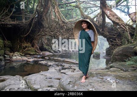 Ein Mädchen aus dem khasi-Stamm in traditioneller Kleidung mit traditionellem Regenschutz aus Bambus, vor einer lebenden Wurzelbrücke, Meghalaya, Indien Stockfoto