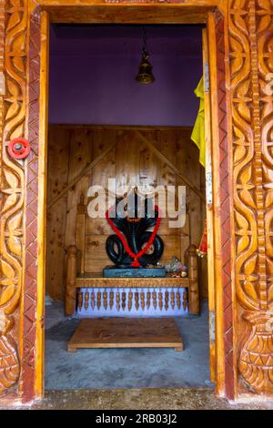 28. Juni 2023, Nagthat, Uttarakhand, Indien. Hindugott Nag Devta oder die Schlangengott-Figur aus schwarzem Stein in einem Tempel mit hölzernem Innenraum. Stockfoto