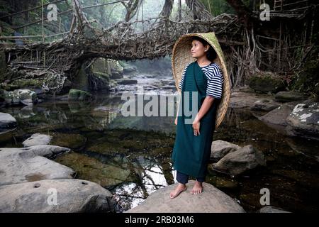 Ein Mädchen aus dem khasi-Stamm in traditioneller Kleidung mit traditionellem Regenschutz aus Bambus, vor einer lebenden Wurzelbrücke, Meghalaya, Indien Stockfoto