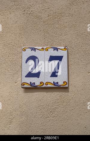 Dekorierte Keramikfliesen 27 Hausnummer auf cremefarbenen rauen Wänden Stockfoto