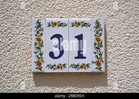 Dekorierte Keramikfliesen, Hausnummer 31, an weißen rauen Wänden Stockfoto