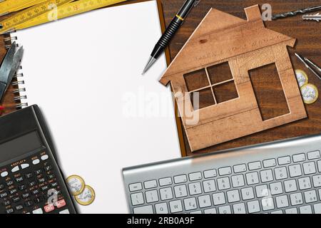 Kleines hölzernes Modellhaus auf einem Schreibtisch mit leerem Notizbuch (Spiralheft) mit Kopierplatz, Taschenrechner, Faltraversen, Arbeitsgeräten, Euro-Münzen. Stockfoto