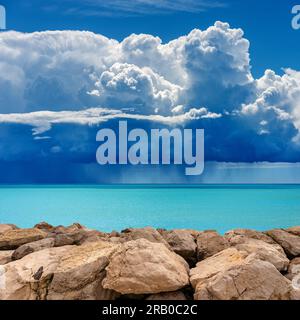 Küste mit Wellenbrecher oder Groyne aus riesigen Felsbrocken und wunderschöne Meereslandschaft mit Sturmwolken (Cumulonimbus) und sintflutartigem Regen. Mittelmeer. Stockfoto