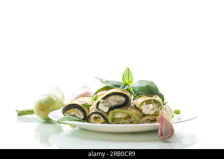 Gekochte Zucchinirollen mit Käse im Inneren, auf einem Teller isoliert auf weißem Hintergrund Stockfoto