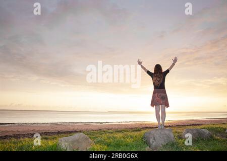 Eine Frau, die am Strand steht, mit ausgestreckten Armen Stockfoto