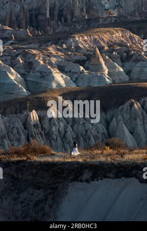 Atemberaubende Aussicht auf eine Person, die während eines wunderschönen Sonnenaufgangs den Blick auf einige Felsformationen im Roten und Rosental in Kappadokien genießt. Stockfoto