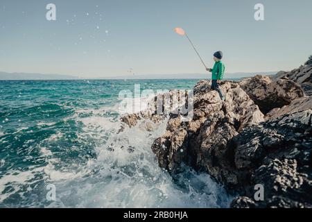 Ein Junge, der mit einem Netz am Festlandufer steht Stockfoto