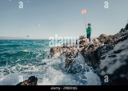 Ein Junge, der mit einem Netz am Festlandufer steht Stockfoto