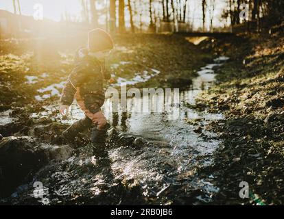 Ein Junge, der durch einen Fluss im Wald rennt Stockfoto