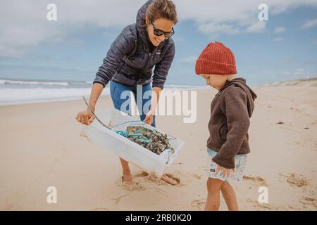 Mutter und Sohn sammeln Müll am Strand Stockfoto