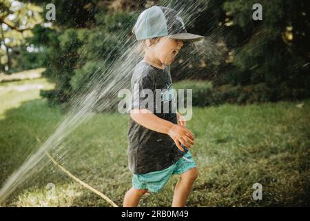 Der Junge wird von Rasensprengern nass Stockfoto