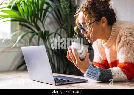 Porträt eines jungen, reifen Unternehmertums, der sein Notebook allein im Büro benutzt und Tee für einen gesunden Lebensstil trinkt. Frauen, die eine Brille tragen und mit einem Computer im Internet surfen Stockfoto