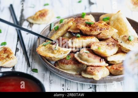 Teller mit goldenen, gebratenen chinesischen Knödeln, auch bekannt als Pot Stickers, mit süßer und saurer Sauce. Selektiver Fokus mit verschwommenem Vorder- und Hintergrund Stockfoto