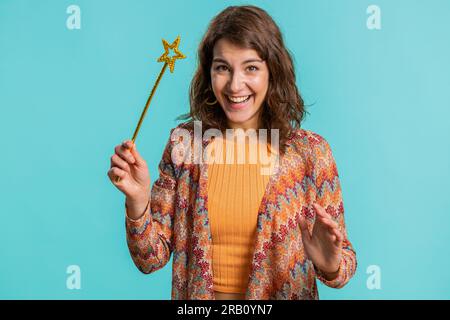 Magier Hexe junge Frau, die mit Zauberstab-Feenstab Gesten macht, Wünsche wahr werden lässt, Zauberspruch ausspricht, Werbeferien-Rabatt. Hübsches Mädchen isoliert auf blauem Studiohintergrund Stockfoto