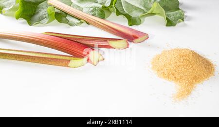 Gesundes Essen. Rhabarberstiele und ein Haufen brauner Zucker auf weißem Hintergrund. Stockfoto