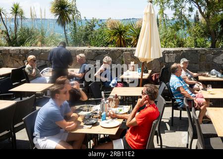 Herm, Kanalinseln, Vereinigtes Königreich. 11June 2023 Urlauber genießen ein Mittagessen vor einem Herm Island Restaurant, Blick auf Guernsey eine andere Kanalinsel. Stockfoto