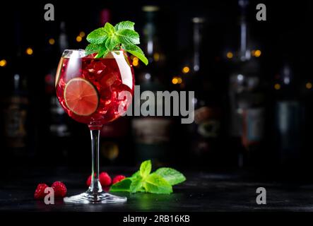 Alkoholische Cocktailgetränke aus königlicher Limonade mit Tequila, trockenem Gin, weißem Rum, Wodka, Likör, Limette, Himbeeren und Eis in Weinglas. Schwarzer Bartresen Ba Stockfoto