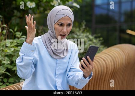 Verärgerte traurige Frau erhielt eine Online-Benachrichtigung mit schlechten Nachrichten, muslimische Frau in Hidschab hält Telefon, benutzt App. Stockfoto