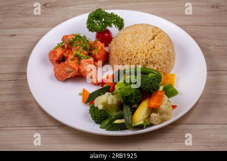 Chicken Tikka Quinoa auf weißem Teller auf Holzhintergrund Stockfoto