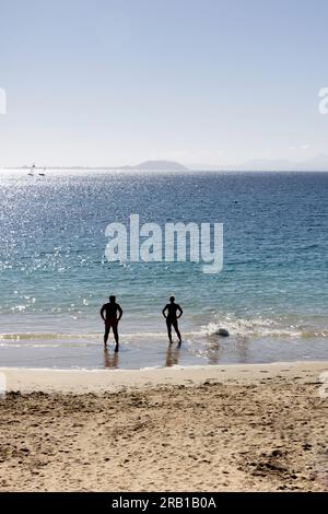 Zwei Touristen stehen am Ufer in Playa Blanke, Lanzarote, mit Blick auf den Atlantischen Ozean Stockfoto