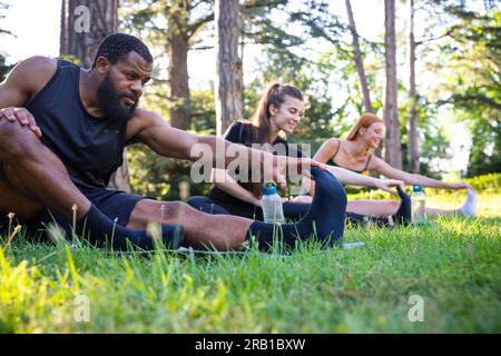 Eine Gruppe von Athleten führt eine Dehnungsübung durch, während sie auf einer Wiese sitzen Stockfoto