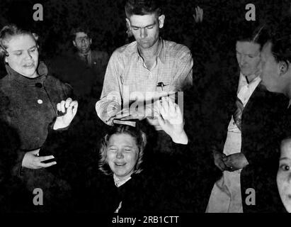 Vereinigte Staaten: c. 1948 Ein Mann legt eine bibel auf den Kopf eines ekstatischen, knienden Gläubigen, der auf den Ruf des Predigers bei einem Revival-Treffen reagiert. Stockfoto