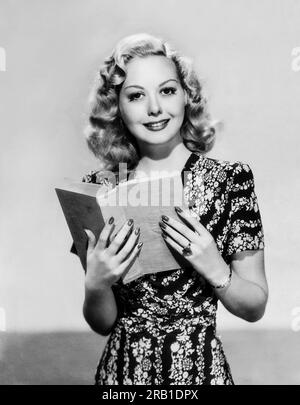 Vereinigte Staaten: c. 1948 Eine junge Frau steht und schaut vom Lesen eines Buches auf. Stockfoto