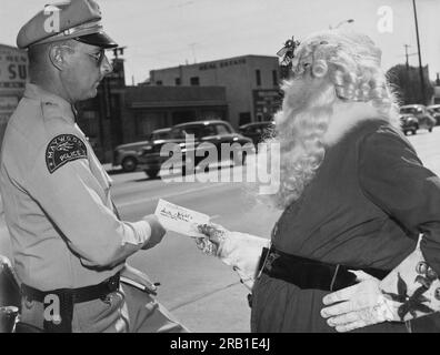 Maywood, Kalifornien: 1952 Santa Claus kann sich keine Pause von der Polizei verschaffen, wenn ein örtlicher Polizist ihm einen Strafzettel ausstellt. Stockfoto