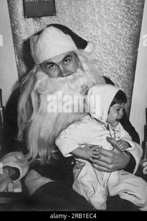 USA: 1951 Ein frustrierter Weihnachtsmann, der ein unglückliches und weinendes Kleinkind auf dem Schoß hält. Stockfoto