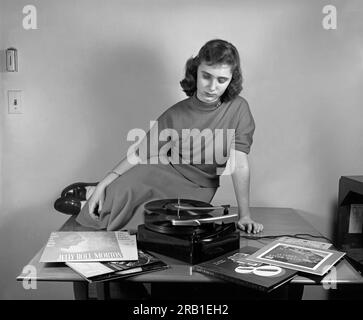 USA: c. 1952 Eine junge Frau, die mehrere Jazz- und Big-Band-Alben auf einem Voice of Music-Phonograph mit einem Multiple-Record-Changer hört. Stockfoto