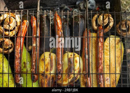 Gebratene Zucchini mit Paprika und Pilzen und Würstchen auf dem Grill im Sommer bei einem Picknick im Park, Gemüse und gegrillte Würstchen Stockfoto