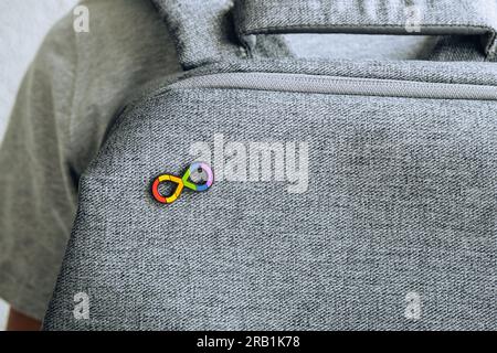 Teenager-Junge mit Autismus-Unendlichkeits-Regenbogensymbol Schild mit metallischer Nadelbrosche auf grauem Rucksack. Welttag des Autismus-Bewusstseins, Autismus-Rechte-Bewegung Stockfoto