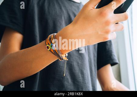 Teenager mit Smartphone. Armband mit Autismus-Unendlichkeits-Regenbogen-Symbol auf seiner Hand. Welttag des Autismus-Bewusstseins, Autismus-Rechte-Bewegung Stockfoto