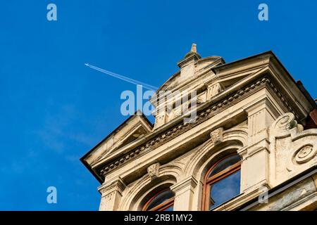 Verlassenes, orangefarbenes Landhaus in der Nachmittagssonne. Über dem Flugzeug hinterlässt ein Kondensat am blauen Himmel Stockfoto