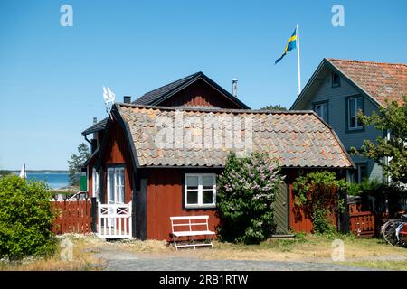 Typisches falu-rotes Haus in Schweden mit weißen Ecken auf einer malerischen ländlichen, historischen Fischerdorfinsel in Stockholmer Inselgruppe mit schwedischer Flagge Stockfoto